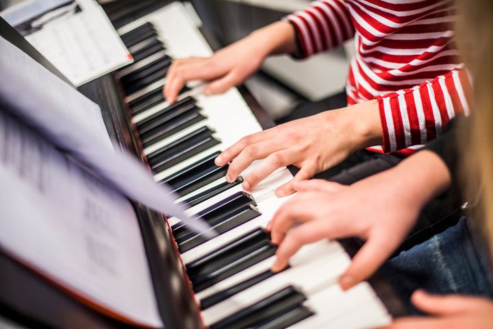 Kaksi henkilöä soittaa yhdessä pianoa.