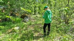 Henkilö seisoo metsässä katsoen kännykkää.