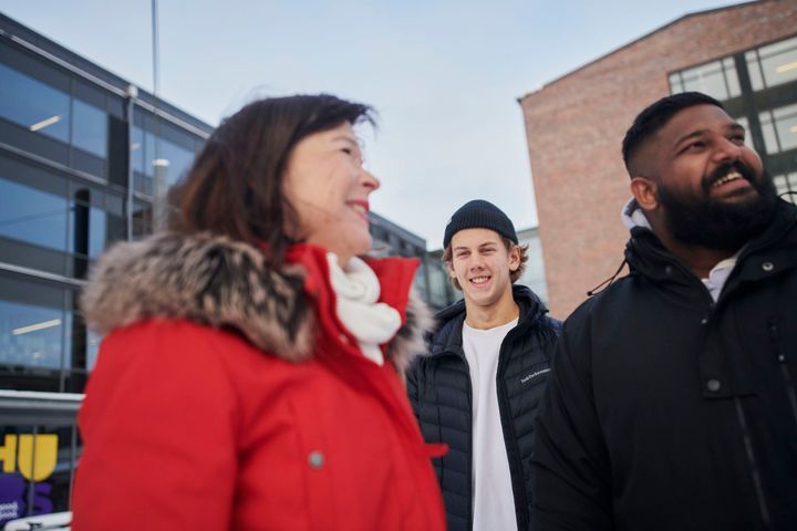 Kolme hyväntuulista henkilöä kuljeskelee Tampereen ammattikorkeakoulun pihalla pilvisenä talvipäivänä.