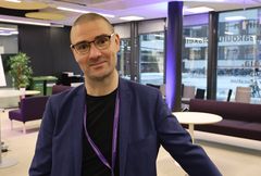 Puvuntakkiin pukeutunut silmälasipäinen mies katsoo kameraan.