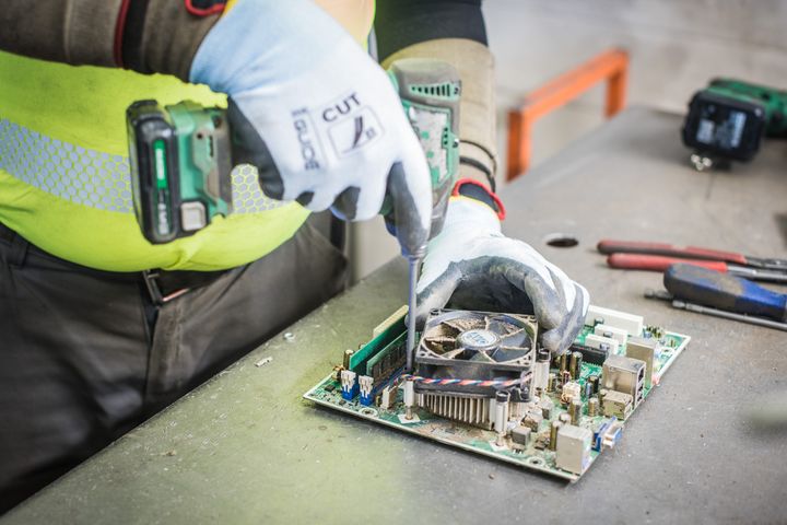 Henkilö työstää piirilevyä ruuvimeisselillä käsineet kädessään.