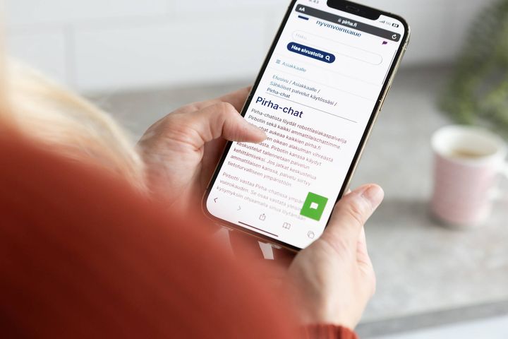 Kuvassa näkyy käsi, joka pitelee kännykkää. Kännykässä avoinna chat-ikkuna.