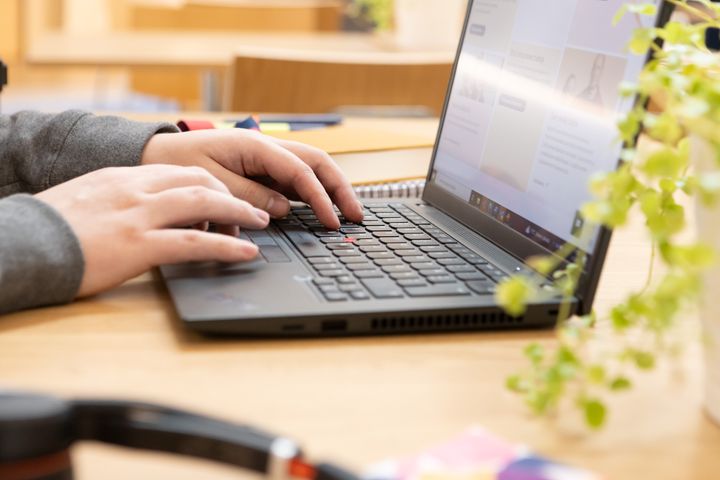 Pöydän ääressä tietokoneella kirjoittava ihminen.