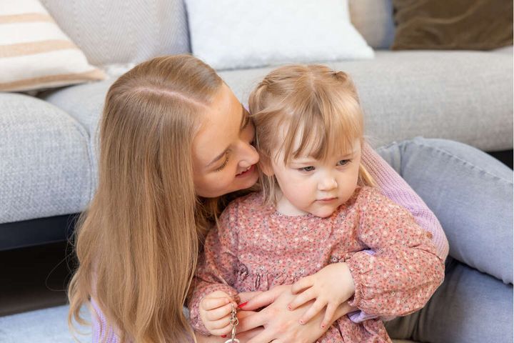 Äiti pitää sylissään ja halaa pientä lasta sohvalla.