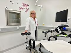 Lääkäri Katja Ahinko seisoo vastaanottohuoneessa ultraäänilaitteen vieressä ja hymyilee.