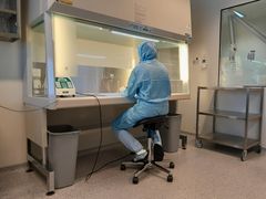 Henkilö työskentelee sinisissä suojavaatteissa laminaarivirtauskaapin ääressä.