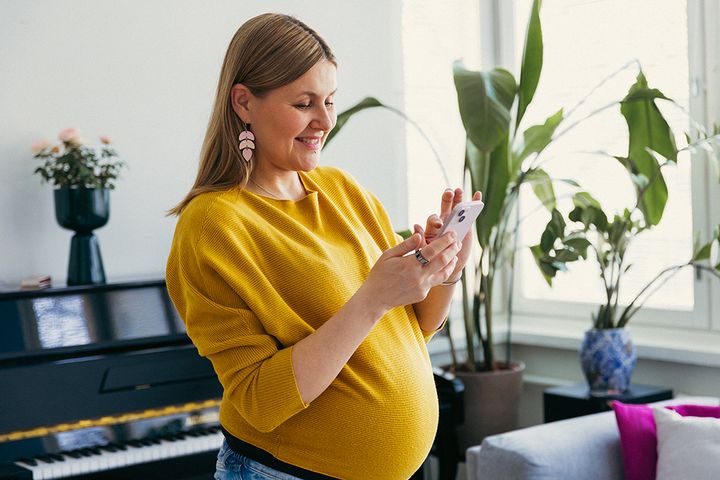 Leende gravid kvinna använder en smartphone.