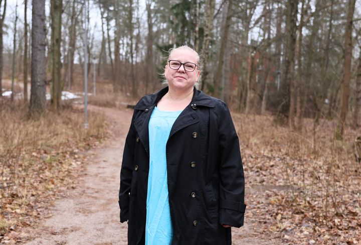 En%20kvinna%20i%20glas%F6gon%20och%20m%F6rk%20kappa%20st%E5r%20p%E5%20en%20stig%20i%20skogen.