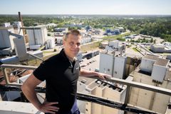 Mies seisoo korkealla katolla, nojaa kaiteeseen ja katsoo kameraan, taustalla avautuu tehdasalue.