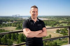 Mies seisoo kädet puuskassa korkealla katolla ja katsoo kameraan, taustalla avautuu kesäistä maastoa.