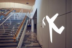 Kuvassa on lentokoneen symboli valkoisella seinällä lentoasemalla, portaiden vieressä.