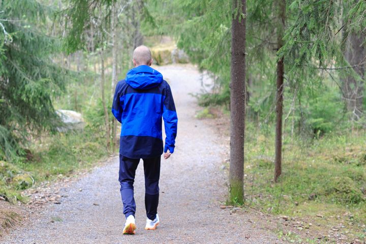 Mies kävelemässä reippaasti metsässä polveilevalla kuntoradalla.