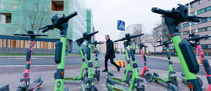 Värikkäitä sähköpotkulautoja kadunvarressa ja niiden takana jalankulkija.