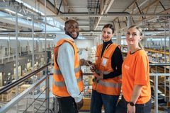 Postin työntekijöitä lajittelukeskuksessa hymyilevät kameralle.