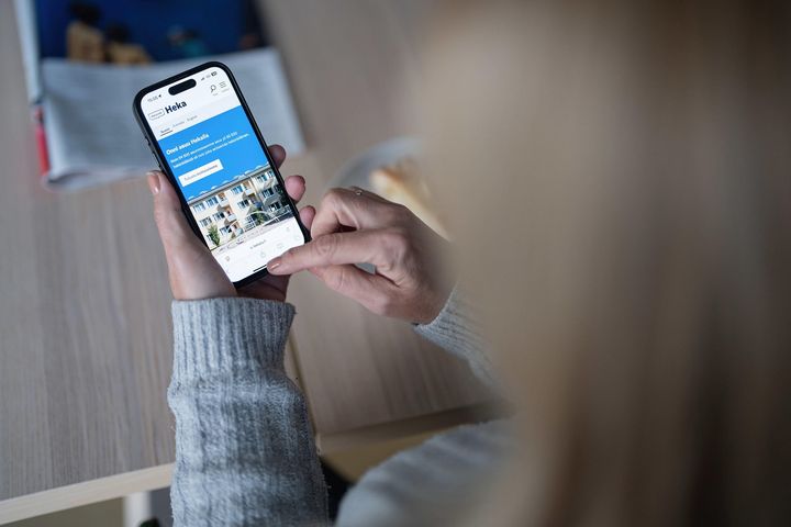 Henkilön kädessä puhelin, jonka ruudussa näkyy OmaHeka.