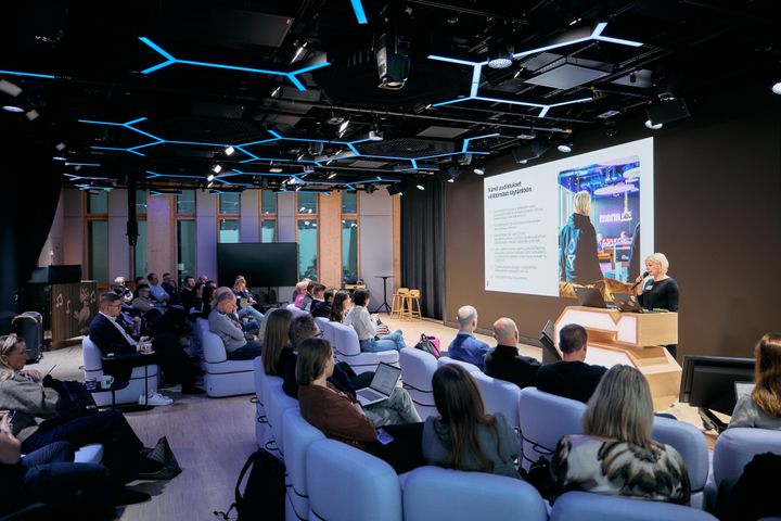 Ihmiset istuvat tilassa ja seuraavat esitystä.