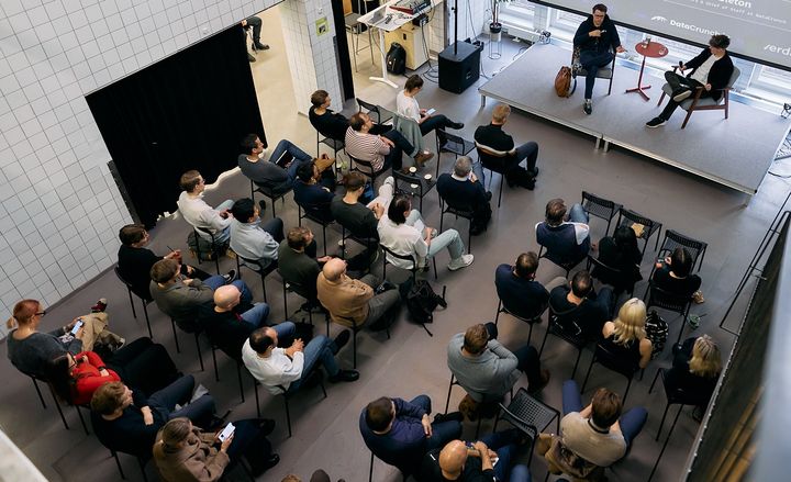Ylhäältä kuvattu näkymä yleisöstä ja kahdesta puhujasta lavalla Suomen Startup-yhteisön tapahtumassa.
