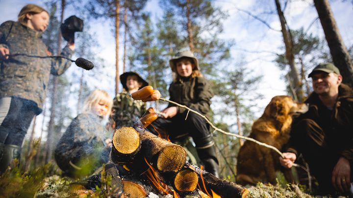 Lapsia ja aikuinen paistamassa makkaraa.