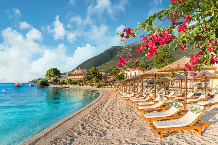 Ranta, jossa on aurinkotuoleja ja värikkäitä kukkia rauhallisen sinisen meren rannalla.