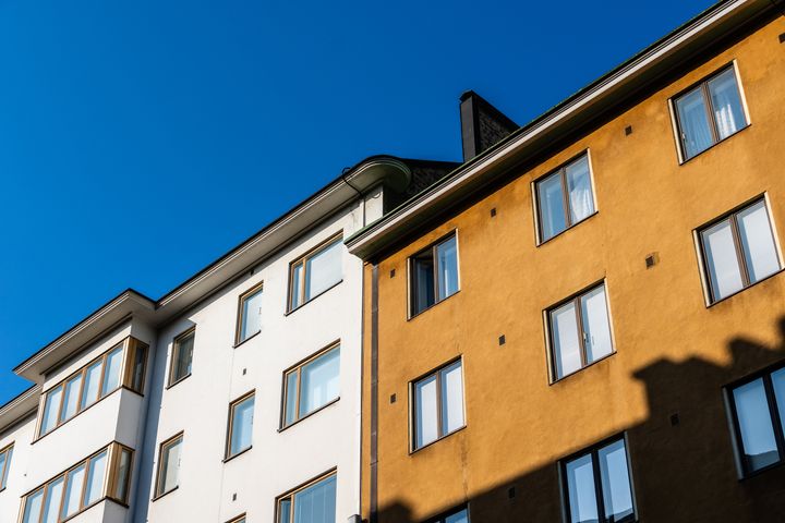 Valkoisen ja keltaisen kerrostalon julkisivu sinistä taivasta vasten.