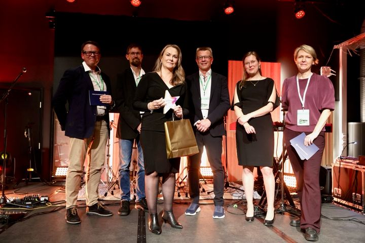 Valinnan julkistuksessa Paikallisliikennepäivien iltajuhlassa Jyväskylän Paviljongissa 17.9.2026 Helena Väliaho kolmas vasemmalta tunnustuspalkinto kädessään. Mukana kuvassa valintaraatia edustavat toimitusjohtaja Vesa Silfver HSL ja joukkoliikennepäällikkö Esa Partanen, Kotkan kaupunki. Helenan oikealla puolella Suomen Paikallisliikenneliitto ry varapuheenjohtaja ja palvelupäällikkö Kari Ström, Jyväskylän kaupunki, Paikallisliikenneliiton puheenjohtaja ja liikennejohtaja Johanna Wallin, HSL ja Paikallisliikenneliiton toiminnanjohtaja Minna Soininen