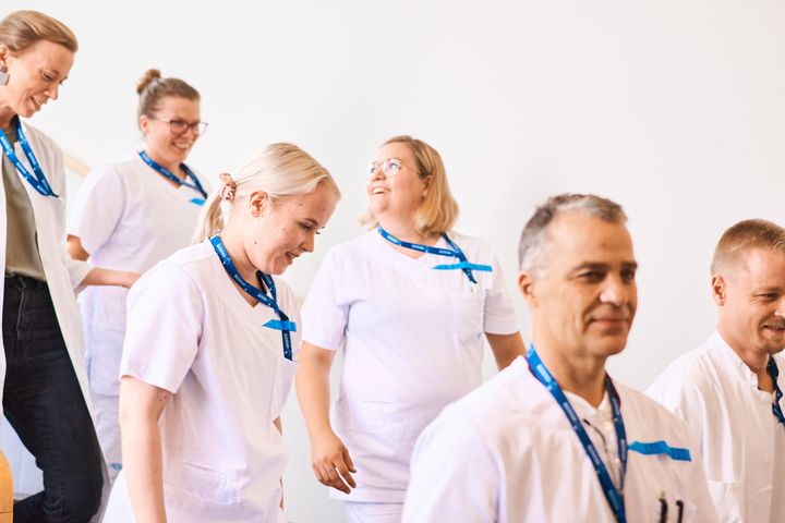 Ryhmä terveydenhuollon ammattilaisia kävelee sisällä ja hymyilee.