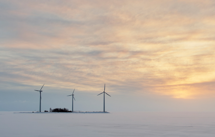 Talvinen maisema, jossa näkyy kolme tuulivoimalaa pienessä saaressa tai luodolla.
