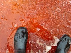 Mustien kumisaappaiden alla verenpunainen jää.