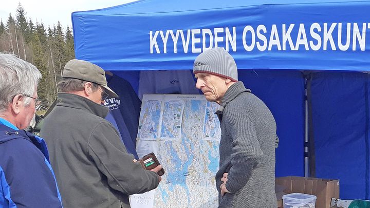 Veijo Lahtinen seisoo Kovalansuon kosteikon avajaistapahtumassa ulkona olevan infoteltan edessä ja juttelee osallistujien kanssa.