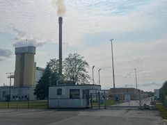 Kuva Forssan lasivillatehtaan sisäänkäynnistä, jossa näkyy korkea savupiippu.