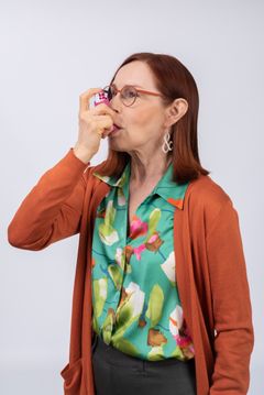 Keski-ikäinen nainen ottaa astmalääkettä inhalaattorilla.