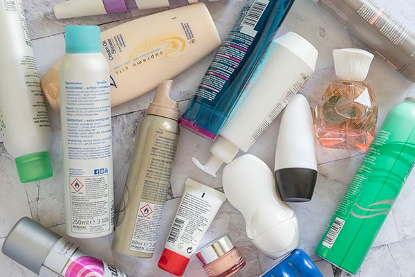 Useita erilaisia kosmetiikkatuotteita pitkällään pöydällä, esimerkiksi hiuskiinne, shampoo, kosteusvoide, deodorantti ja silmänympärysvoide.