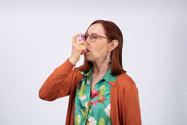 Keski-ikäinen nainen vetää henkeen astmalääkettä inhalaattorilla.