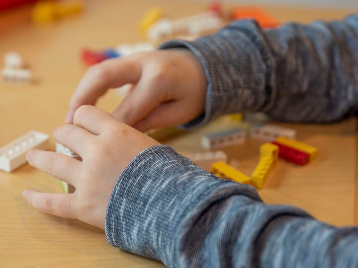 Lapsi leikkii pöydällä värikkäillä Lego-palikoilla.
