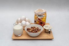 Kulhollinen pähkinöitä, kananmunia, maitolasi ja vehnäjauhopussi puisella alustalla.