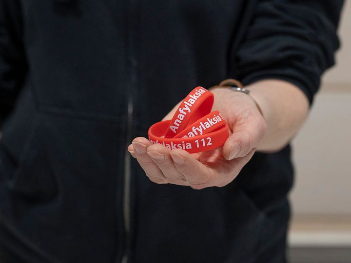 Henkilö pitelee punaista ranneketta, jossa lukee "Anafylaksia 112".