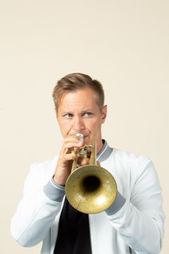Jukka Eskola soittaa trumpettia vaaleanruskean taustan edessä.