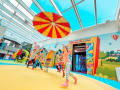 Lapset leikkivät värikkäässä sisähuvipuistossa, jossa on sateenvarjon muotoinen katos ja värikäs seinä.