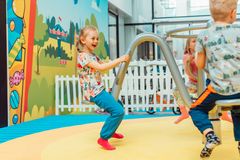 Kolme lasta leikkii värikkäässä sisäleikkipuistossa. Taustalla on piirrosmaisia kuvia ja valkoinen aita.