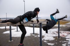 Kaksi henkilöä kiipeilee puupalkin yli ulkona talviasussa. Taustalla talvinen maisema.