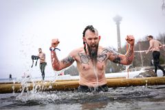 Mies tuulettaa voitonriemuisesti estejuoksukilpailussa kylmässä vedessä. Taustalla näkyy Tampereen maamerkkejä.