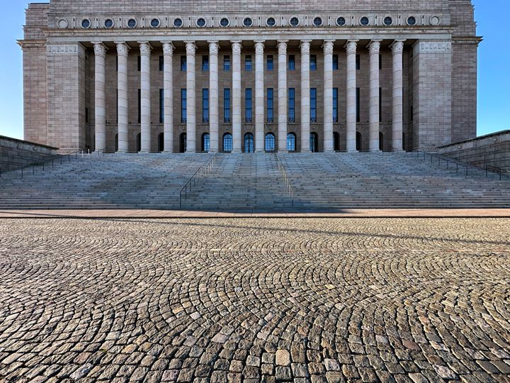 Eduskuntatalo paraatipuolelta kuvattuna, edessä hiekkakenttää