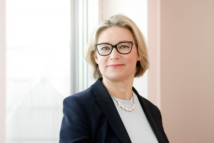 Nainen mustassa jakussa katsoo kameraan.