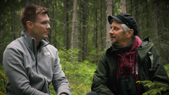 Kaksi miestä keskustelee metsässä istuen.