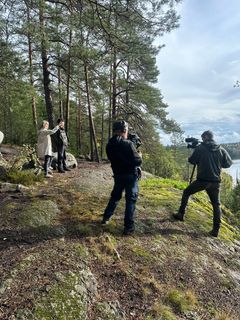 Kolme henkilöä metsäisessä maisemassa kuvaamassa dokumenttisarjaa.