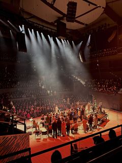 Näyttämöllä orkesteri esiintymässä konserttisalissa, yleisö istumassa katsomossa.