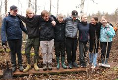 Ryhmä nuoria seisoo vierekkäin ulkoilmassa metsässä leveällä pitkospuulla.