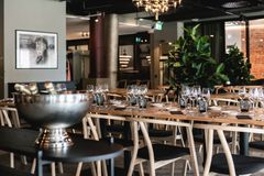 Tyylikäs ravintola- ja juhlatila, jossa modernit puiset kalusteet, viherkasveja ja tunnelmavaloja.