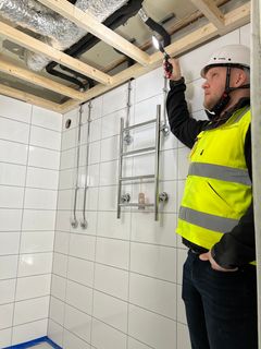 Kuvassa Remonttipartion myyntijohtaja Jaakko Hartikainen kypärä päässä ja huomioliivi yllä. Hän on remontoitavassa kylpyhuoneessa ja katsoo sen auki olevia kattorakenteita valolla.