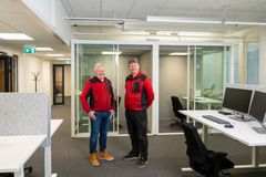 Ilkka Okkonen ja Pasi Jakonen uusissa toimistotiloissa. Heillä on yllään punaiset pusakat ja molemmat hymyilevät. Taustalla näkyy kaksi lasiseinäistä työhuonetta.